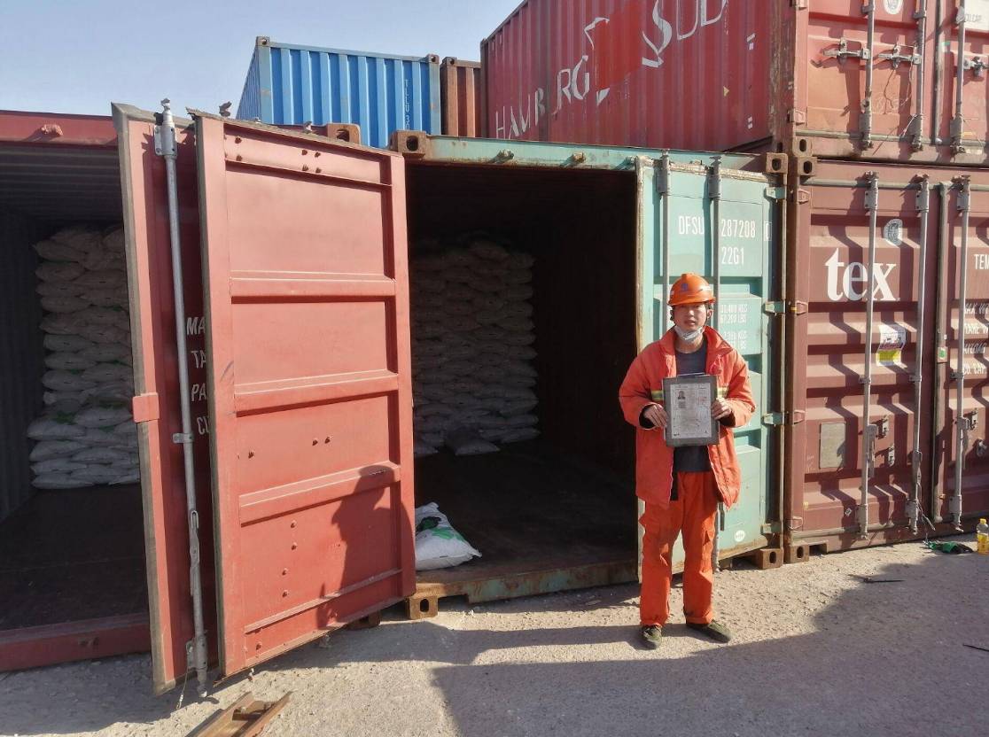 Worker holding a certificate in front of an open shipping container loaded with battery chemicals from Camachem.