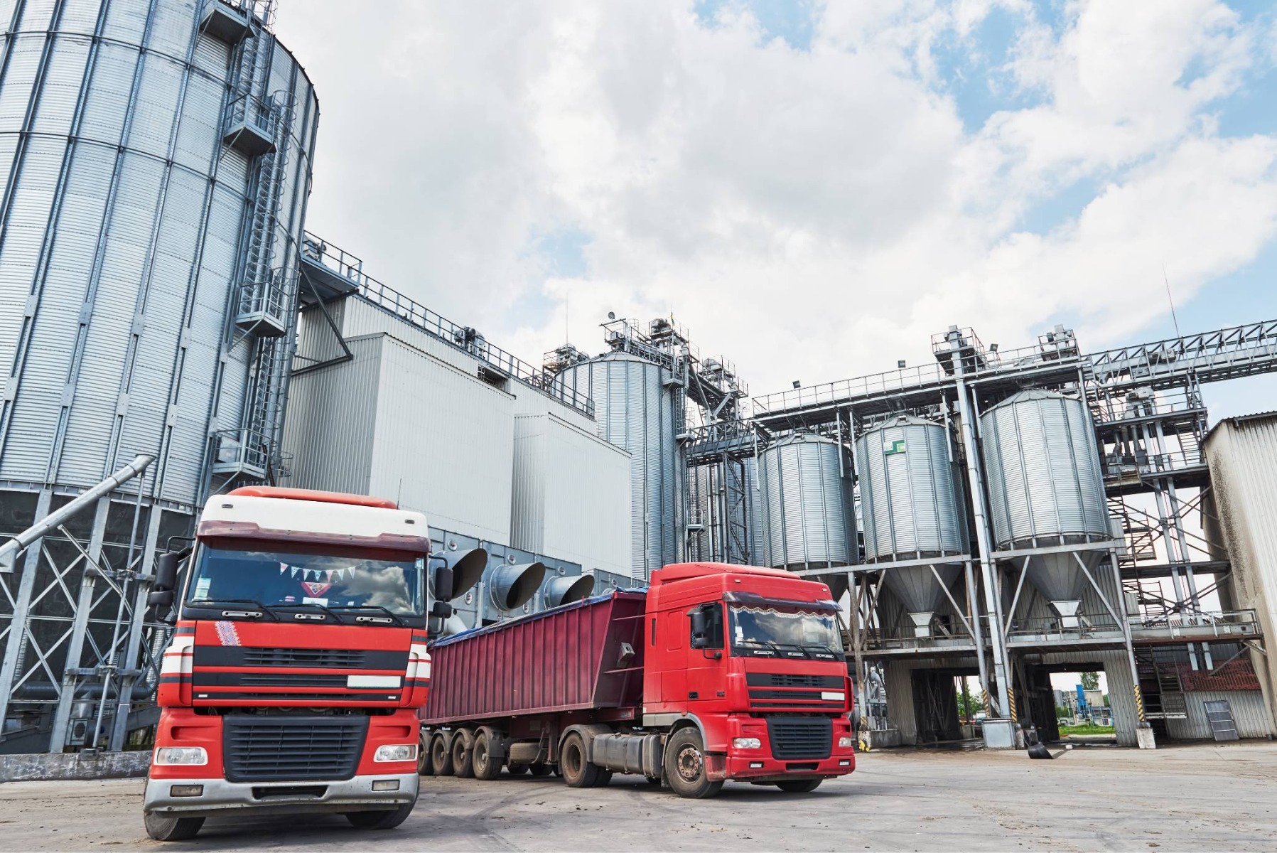 Red freight trucks at an industrial chemical plant, representing battery chemical logistics and supply chain infrastructure