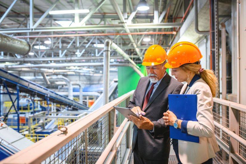 Image of an inspection taking place in a manufacturing factory, with two workers discussing the process while reviewing a board sheet.